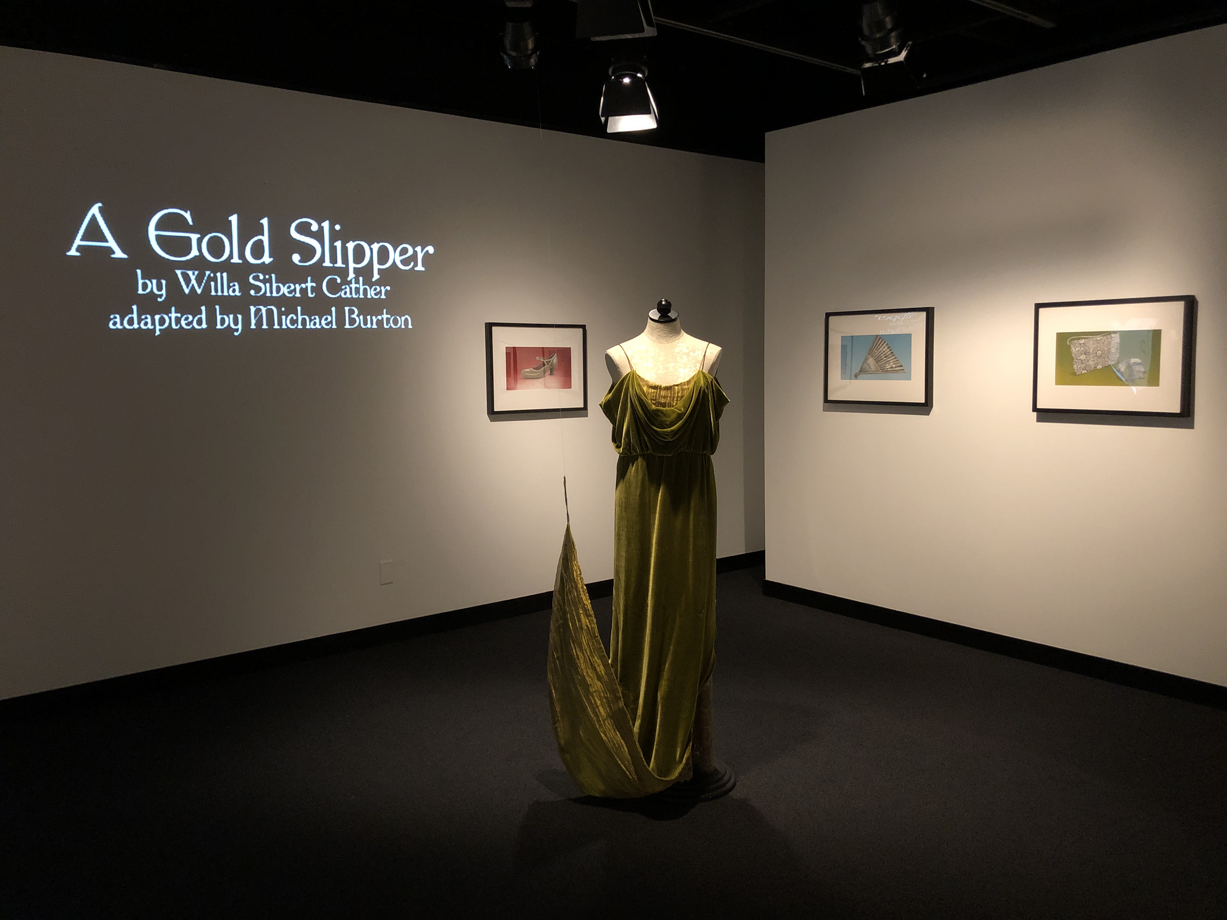 Image with a green-gold velvet dress in the center of the screen and the title of the exhibit to its left.